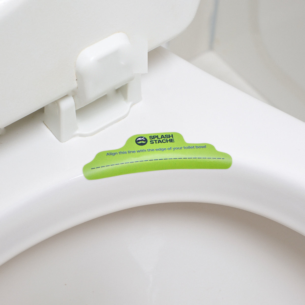 Green Splash Stache alignment sticker placed on the back rim of a white toilet bowl, dotted line running along the edge